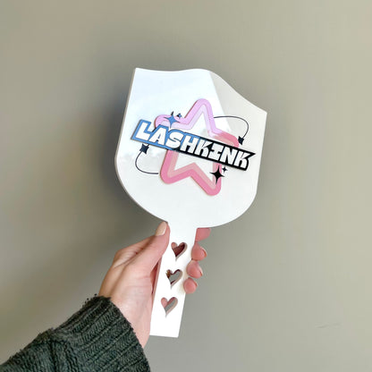 A hand holding a white acrylic handheld mirror with a custom logo printed on it