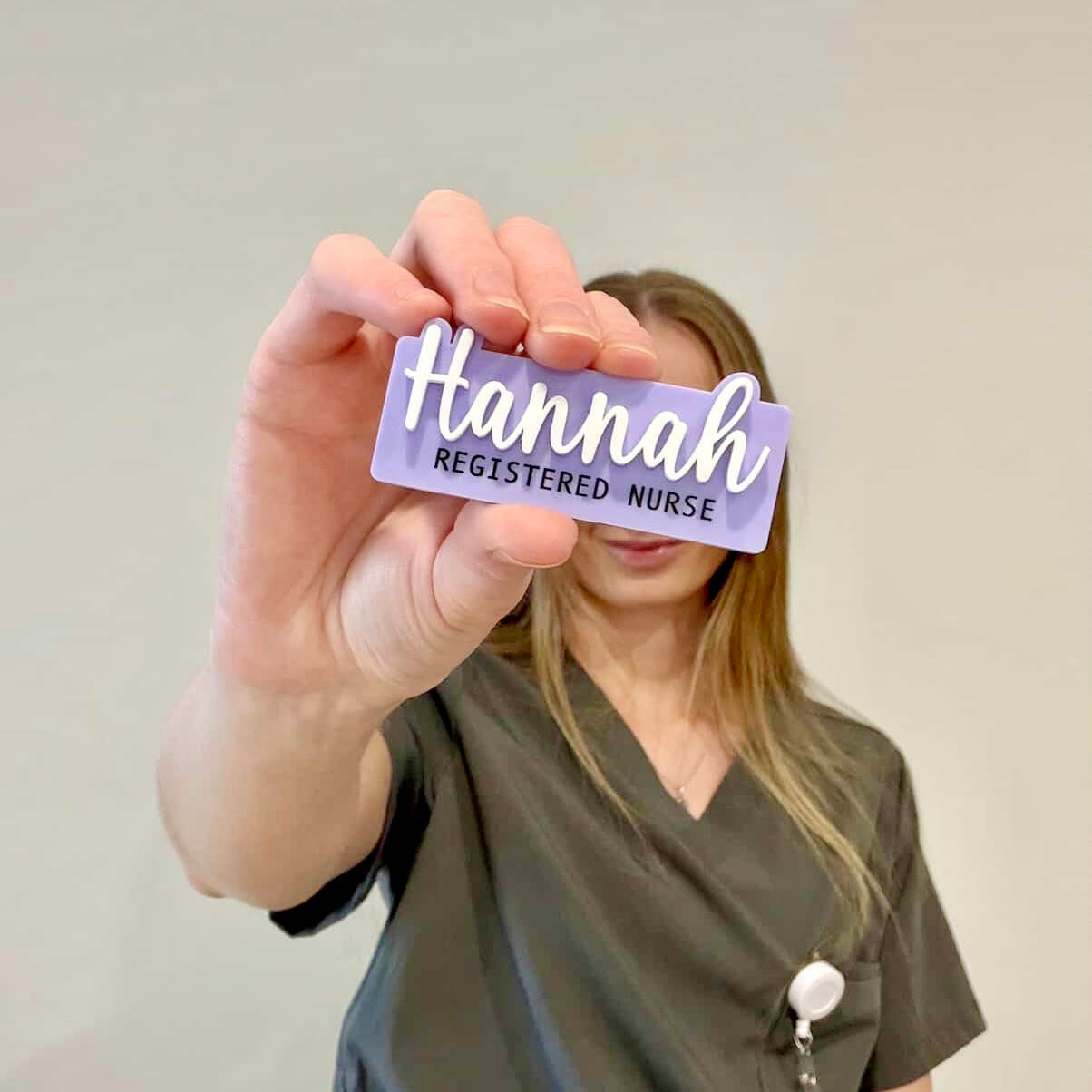Person wearing green scrubs holding a name tag with 'Hannah Registered Nurse' text.